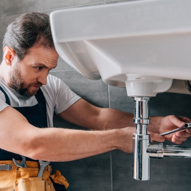 A plumber is working on the pipes underneath a sink.